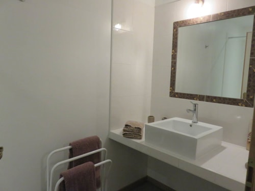 Salle de bain moderne au gîte Sylvie Cambon à Montséret avec vasque blanche, miroir encadré, douche et porte-serviettes.