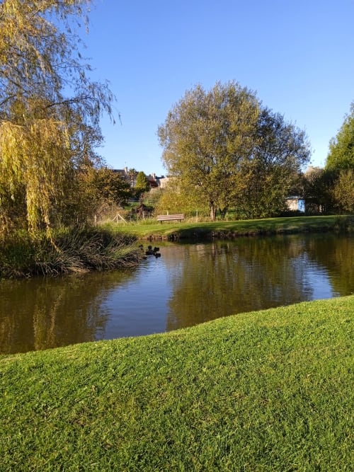Parc riverside pittoresque aux Clématites en Cotentin avec saules pleureurs, pelouse verdoyante et pont de pierre à Saint-Floxel