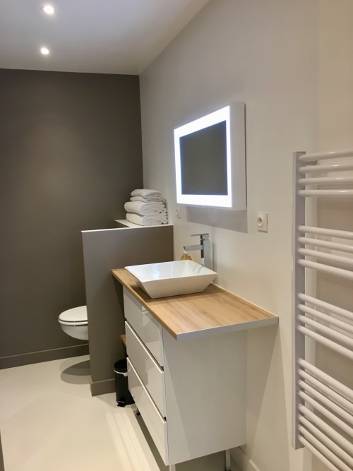 Modern bathroom at Les Maisons de Chamirey cottage with white vanity, vessel sink, illuminated mirror, and heated towel rack