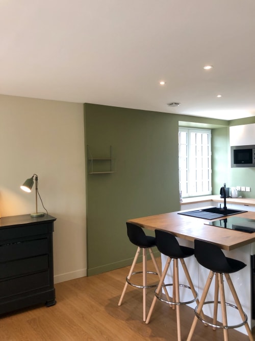 Modern cottage kitchen and dining area with green accent wall, wooden bar seating, and TV at Les Maisons de Chamirey in