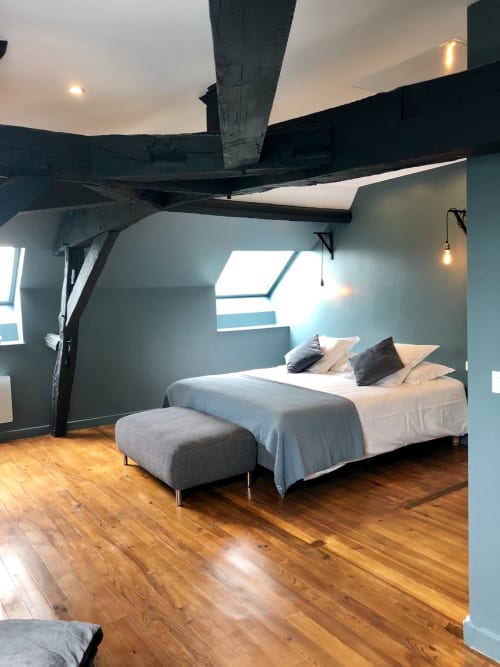 Modern loft bedroom with exposed beams, blue walls, wooden floors, and skylight in Mercurey cottage