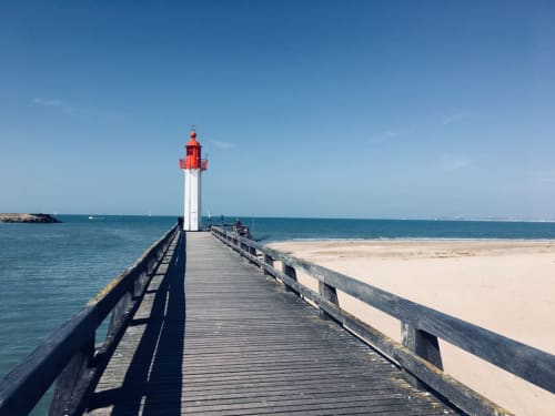 Phare rayé rouge et blanc au bout d'une jetée en bois s'avançant dans les eaux turquoise de l'océan