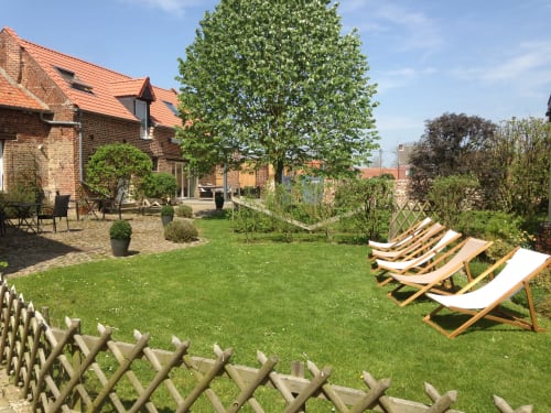 Sunny garden at La ferme de l'Ostrevent B&B with deck chairs, green lawn, brick cottage, and blooming trees in Estrées,