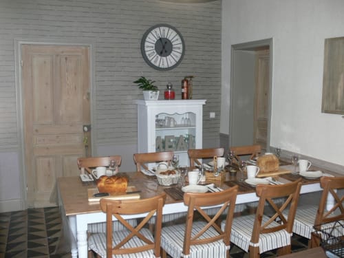 Dining room at Chambres d'hôtes La ferme de l'Ostrevent with wooden table, cross-back chairs, fireplace, and large clock