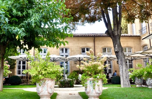 Elegant courtyard at Provence Km28 B&B in Gordes with stone urns, flowering plants, umbrellas, and traditional architecture.