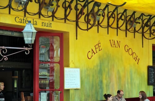 Café Van Gogh exterior in Gordes, France with yellow walls, red door, and wrought iron details near Provence Km28 B&B
