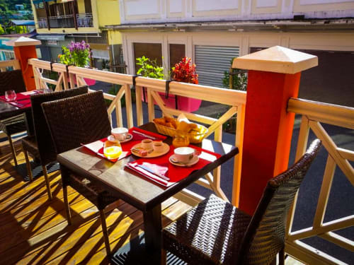 Terrasse ensoleillée de l'Hôtel du Cirque à Cilaos avec mobilier coloré, fleurs en pots et petit-déjeuner