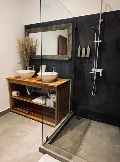 Salle de bain moderne du lodge Organica Yoga Shelter avec vanité en bois, deux vasques blanches, mur d'accent noir, douche pluie