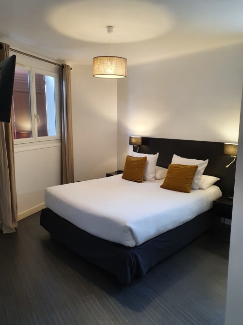 Chambre Junior Suite moderne de l'Hôtel Au Bon Coin à Biarritz avec tête de lit noire, linge blanc, coussins dorés et luminaire suspendu