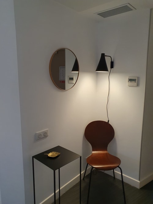 Coin de chambre d'hôtel moderne avec miroir rond, chaise en bois, table basse noire et appliques murales à l'Hôtel Au Bon