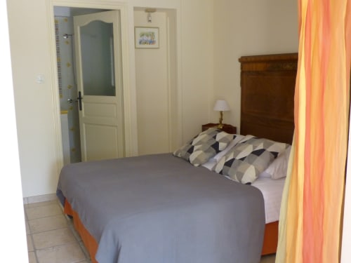 Bedroom at Villa Thébaïde with double bed, wooden headboard, geometric pillows, and orange curtains in Laudun L'Ardoise