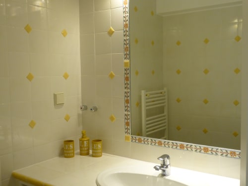 Modern bathroom at Villa Thébaïde with white tiles, gold diamond accents, mirror, sink and heated towel rack