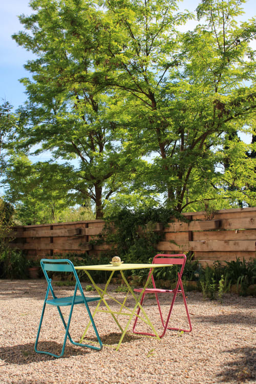 Coin détente coloré du gîte Sylvie Cambon à Montséret avec table de bistrot et chaises sous de beaux arbres verts