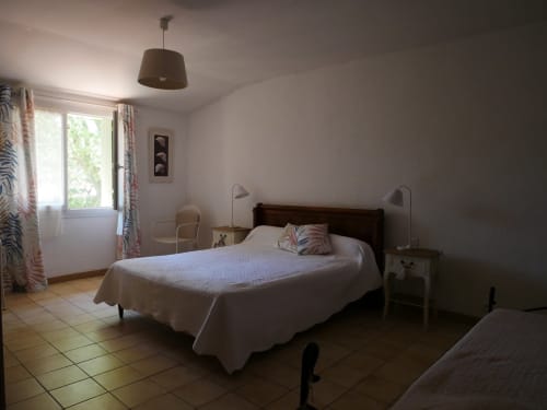 Chambre lumineuse avec lit en bois foncé, draps blancs et vue sur le jardin au Gîte Sylvie CAMBON à Montséret, France