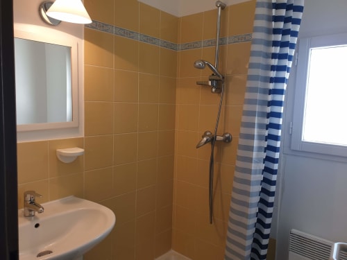Salle de bain moderne avec carrelage doré, douche, lavabo et rideau à rayures bleues à Locmaria Belle-île-en-Mer