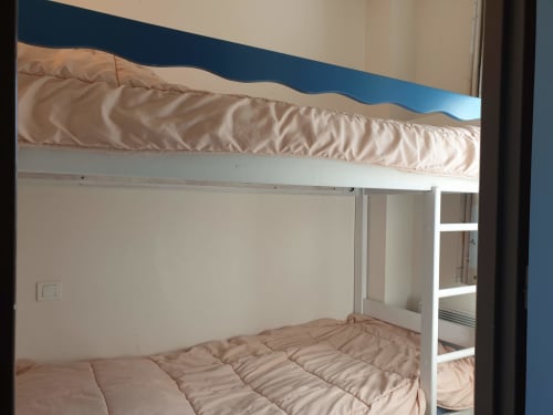 Lits superposés blancs avec literie beige dans une chambre lumineuse avec mur bleu à Loc'Maria, Belle Île en Mer