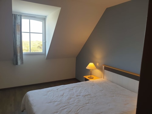 Chambre mansardée lumineuse avec lit aux draps blancs, lampe jaune, vue sur Locmaria à Belle-Île-en-Mer
