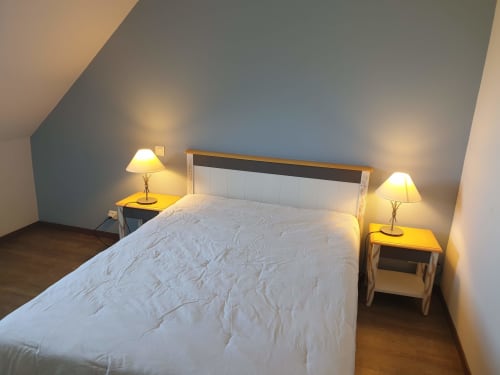 Chambre mansardée douillette avec literie blanche, tables de nuit en bois, lampes jumelles et murs bleus inclinés à Loc'Maria, Belle Île en Mer