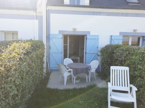 Terrasse de la Résidence 43, Locmaria Belle-Île-en-Mer, avec table ronde, chaises blanches, haies et accès à la vue sur mer