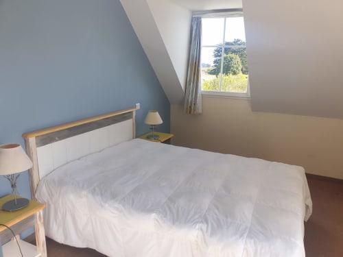 Chambre lumineuse sous les combles avec mur bleu, lit blanc et vue sur le jardin à Locmaria, Belle-Île-en-Mer