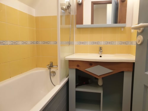 Salle de bain aux carrelages jaunes, lavabo blanc, meuble-vasque en bois et baignoire de l'appartement Loc'Maria Belle Île en Mer