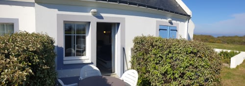 Exterior du gîte blanc Locations Loc'Maria, Belle Île en Mer, avec volets bleus, haies et terrasse vue sur jardin