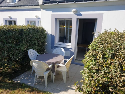 Patio ensoleillé avec table et chaises blanches, entouré de haies vertes à l'appartement Loc'Maria à Belle-île-en-mer