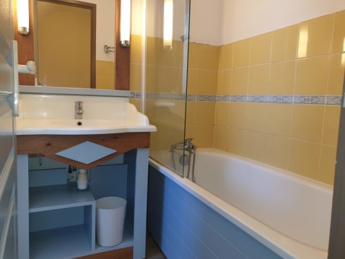 Salle de bain aux carrelages jaunes, baignoire bleue, lavabo blanc et miroir de l'appartement Locmaria