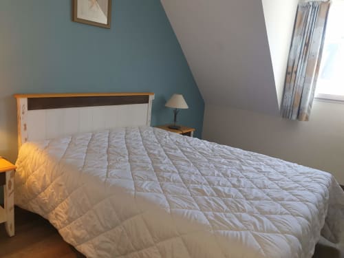 Chambre lumineuse avec lit matelassé blanc, structure bois, mur d'accent bleu-vert et plafond mansardé à Belle-Île-en-Mer