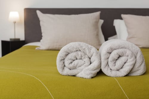 Twee opgerolde handdoeken op geel beddengoed in de St Andoche-kamer van het Moulin Renaudiots hotel in Autun, met witte kussens en hoofdeinde