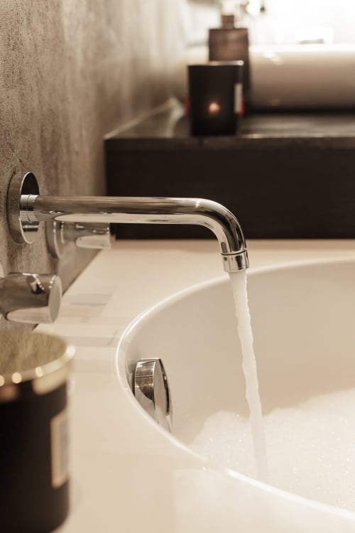 Chromen wandmontage kraan met stromend water in een wit bekken in een moderne badkamer van hotel Moulin Renaudiots, Autun