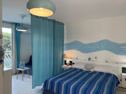 Studio avec rideaux bleu-vert, literie rayée bleue, décoration murale thème océan et éclairage moderne chez Caribluewave