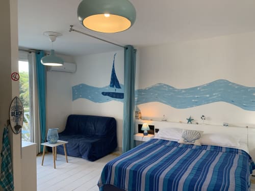Studio côtier Caribluewave avec décor nautique, linge de lit rayé bleu, canapé foncé et luminaires suspendus