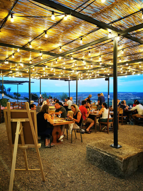 Terrasse de restaurant en plein air chez Sylvie CAMBON avec guirlandes lumineuses, vue panoramique sur la vallée, clients savourant le dîner en soirée