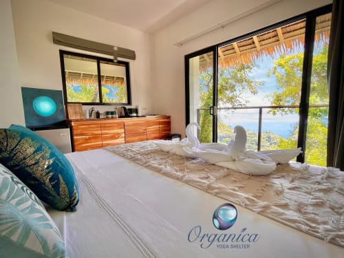 Chambre de luxe en retraite yoga avec vue sur l'océan, cygnes en serviettes blanches, commode en bois et balcon face à la mer à Organica Yoga