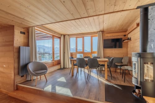 Modern wooden interior of the CosyArc Lauzières apartment in Arc 1800 featuring a dining table, stove, and mountain views through large windows"