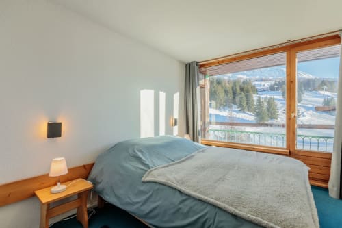 Double bedroom of the CosyArc Lauzières ski apartment in Arc 1800 with double bed, balcony access, and mountain views