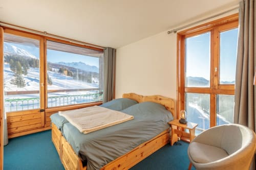 Bright bedroom of the CosyArc Lauzières apartment in Arc 1800 with wooden bed, balcony and views of the mountains and alpine landscape