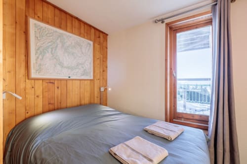 Mountain-view bedroom at Cosyarc Lauzières  in Arc 1800  with wood-paneled walls, bed, balcony access, and Alpine scenery.