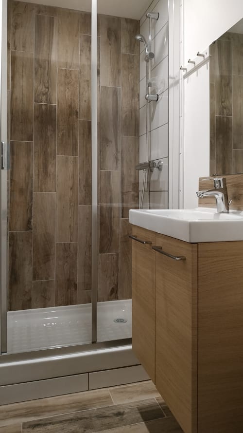 Modern bathroom in Gîte Le Relais Viennois cottage, Blois, featuring wood-grain tile shower, white sink vanity, and chrome
