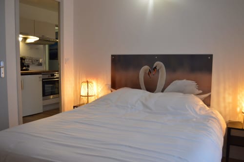 Cozy bedroom at Locacharme cottage in Blois with white bedding, swan artwork headboard, and kitchenette with warm lighting.