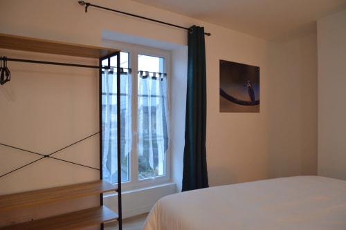 Modern bedroom at Locacharme cottage in Blois with river view, wooden bed frame, dark curtains, and natural light from glass