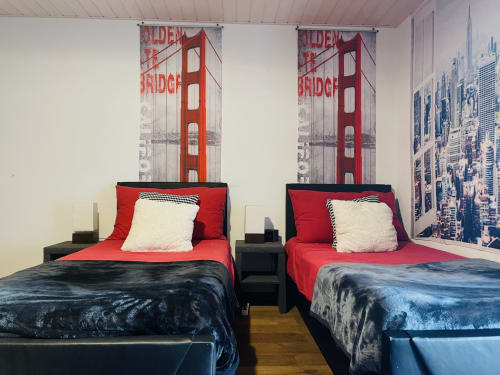 Twin beds with red bedding and San Francisco Golden Gate Bridge wall art in cottage bedroom at Au P'tit Bonheur, Lausanne