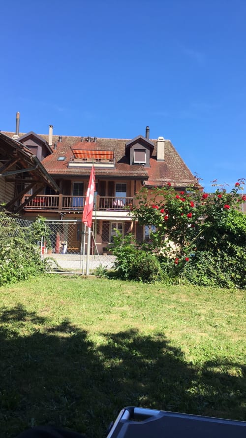 Rustic Swiss chalet with red roof, wooden balcony, and blooming red roses in garden at Au P'tit Bonheur B&B,