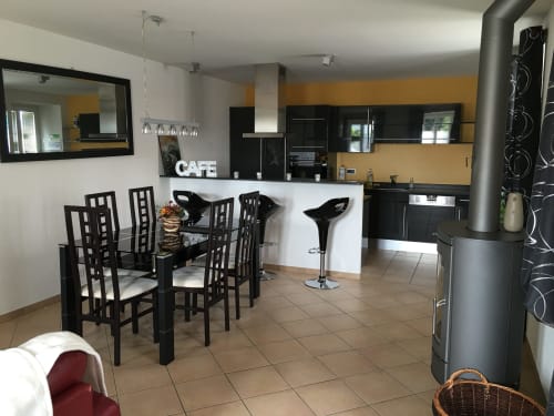 Modern dining area with black chairs, kitchen counter, and gold accent wall at Au P'tit Bonheur cottage in