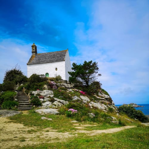 White chapel on rocky hilltop with flowers, Pleyber-Christ Brittany coastal view