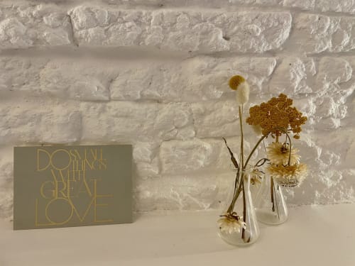 Dried flowers in glass vases beside sage-colored card reading 'Do Small Things with Great Love' at Maison Monsieur Léger