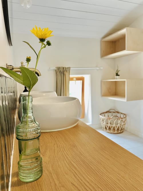 Vanité de salle de bain avec fleur jaune en vase vert, lavabo blanc, comptoir en bois et rangements à la Maison Monsieur Léger
