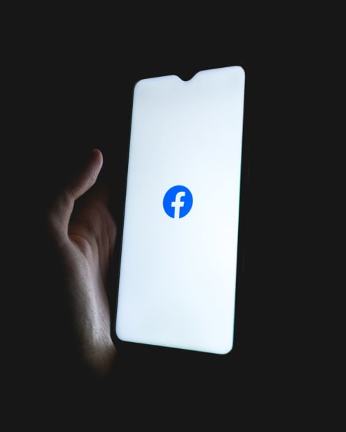 Hand holding smartphone with Facebook logo on screen, Isigny-sur-Mer