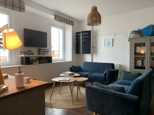 Coin salon contemporain aux fauteuils bleus, tables en bois, vue sur mer et équipements de divertissement aux Filles